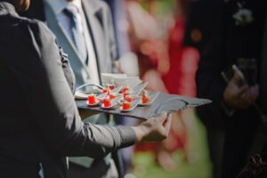 A person holding an umbrella and tray of food.