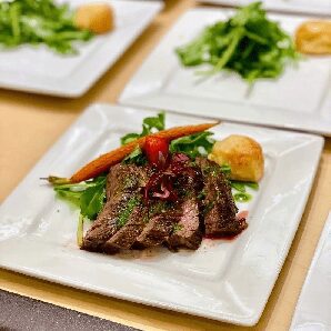 Sliced steak with greens and bread roll.